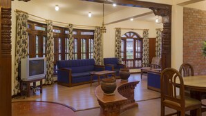 Una sala de estar acogedora con un sofá azul, una mesa de centro de madera y un televisor. Hay cortinas estampadas y una pared de ladrillo.