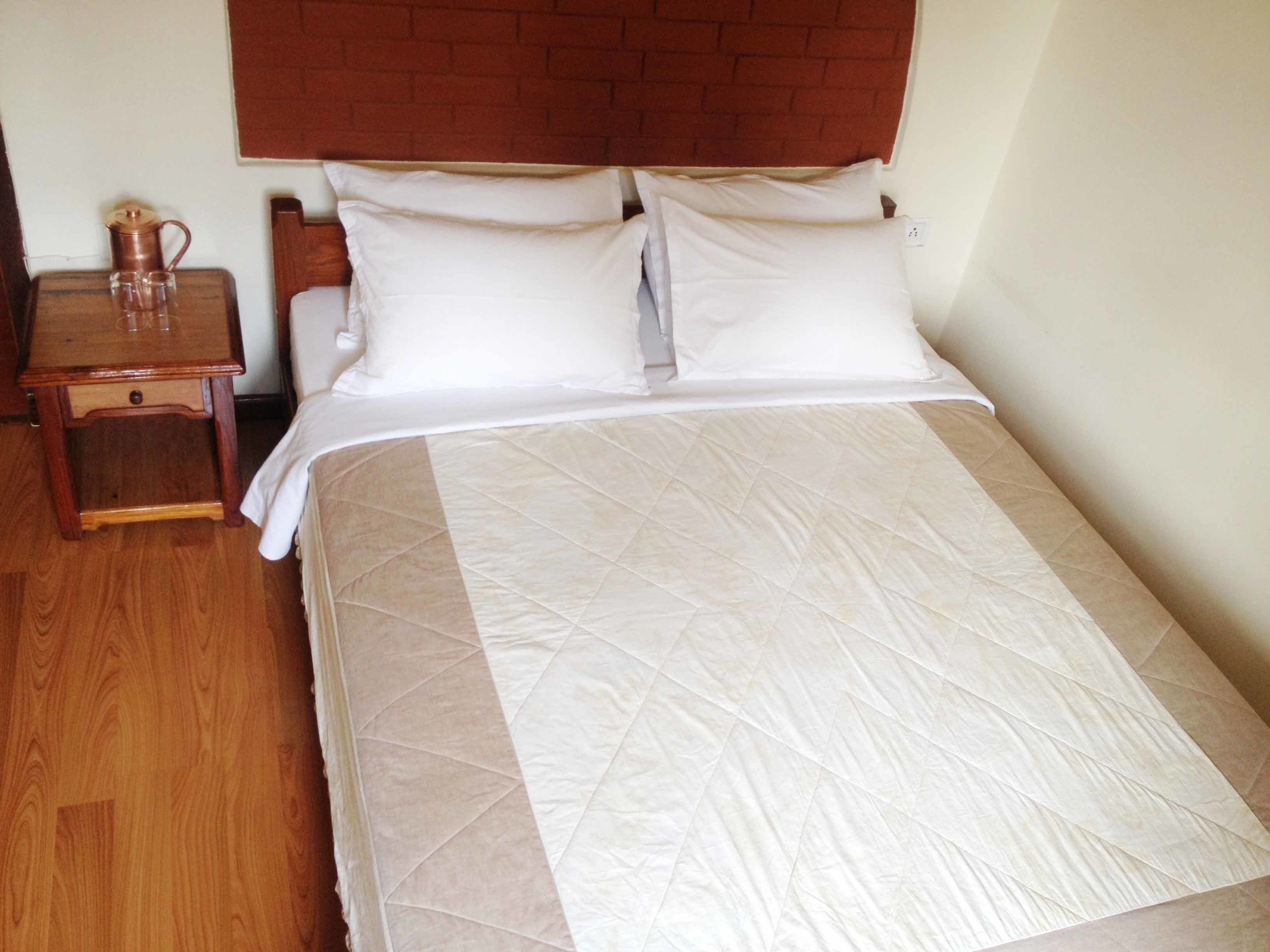 A neatly made bed with a quilted cover, a wooden nightstand with a lamp, and a brick-patterned headboard.