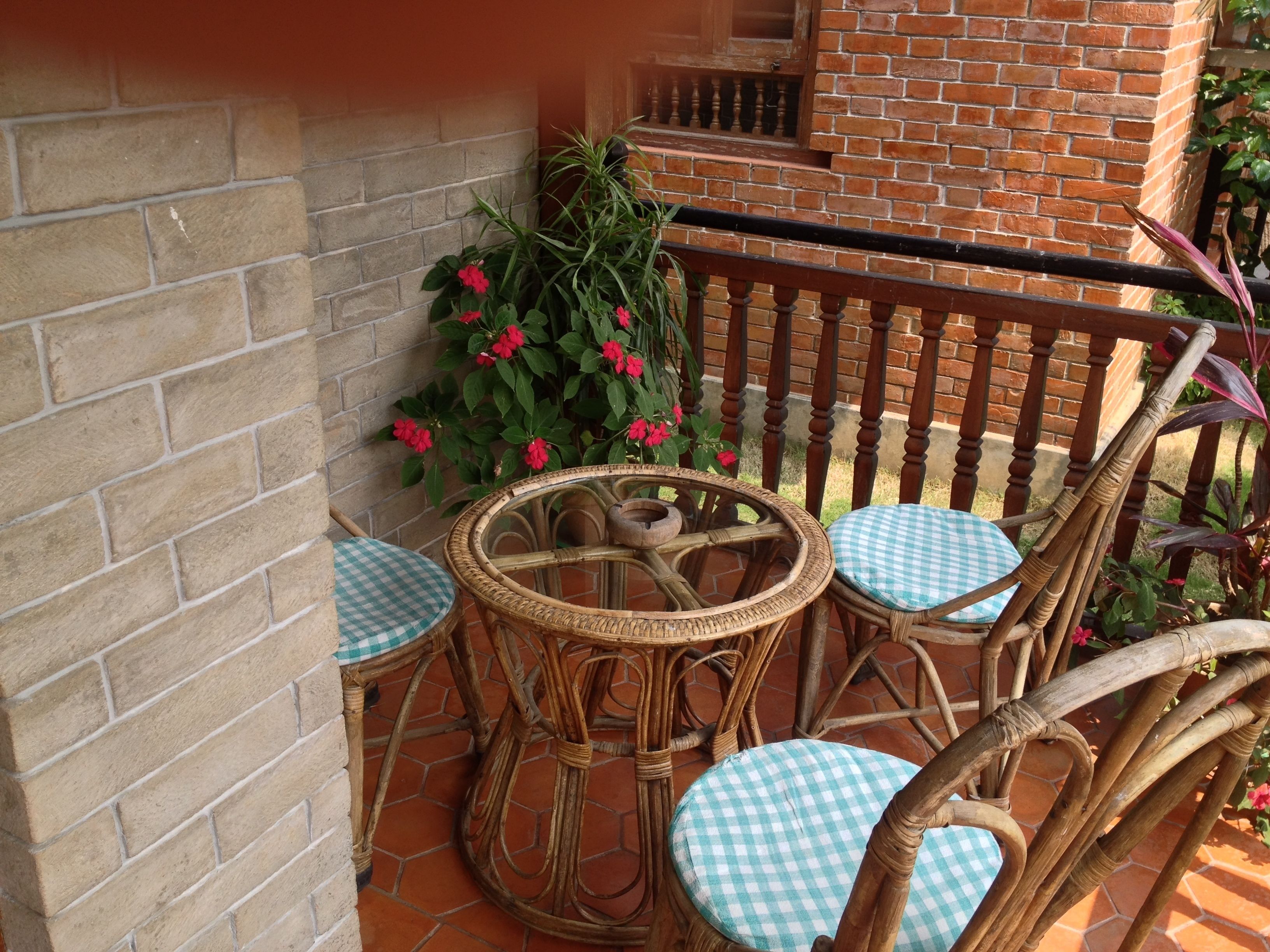 Ein Korbstuhl-Set mit karierten Kissen auf einer gefliesten Terrasse.