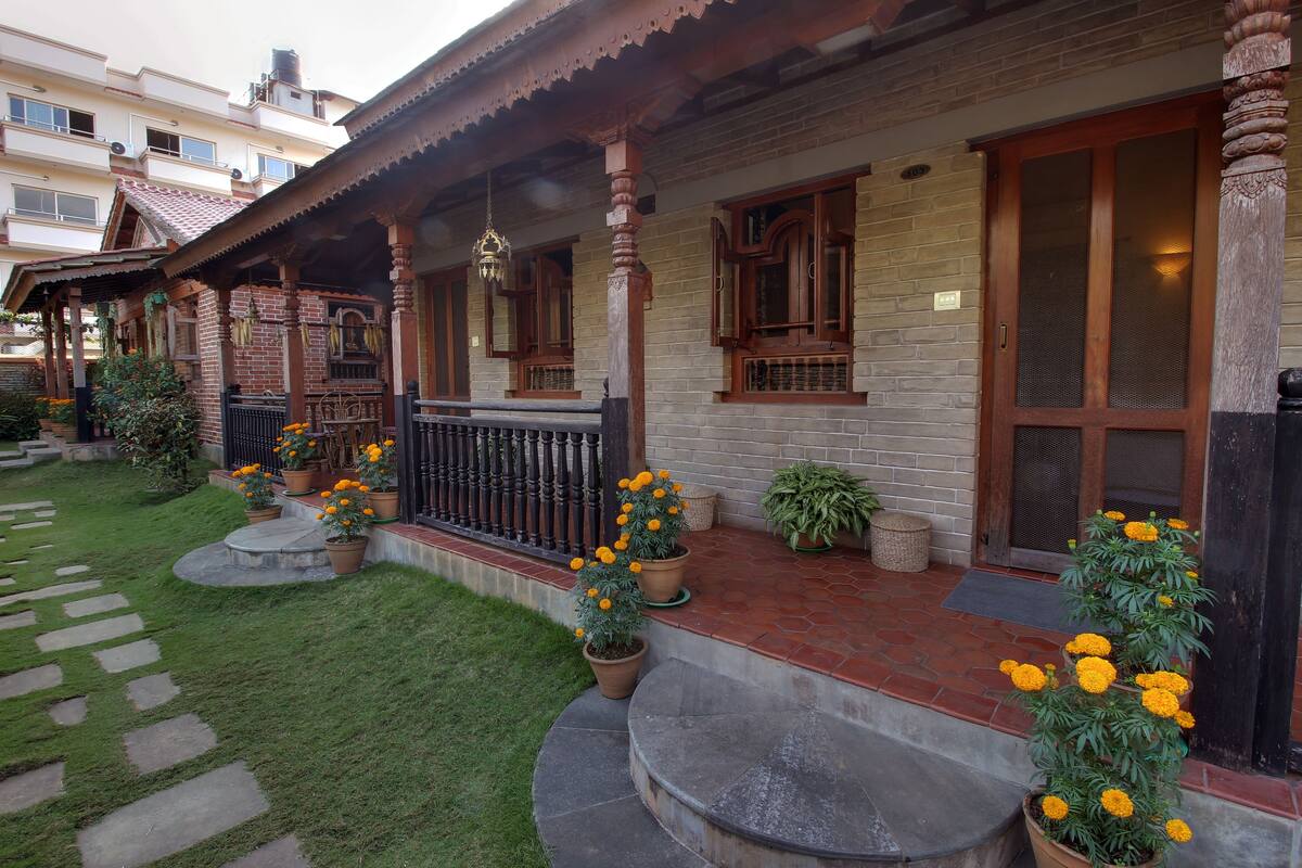 Een traditioneel huis met een veranda, plantenpotten en een keurig onderhouden tuin.