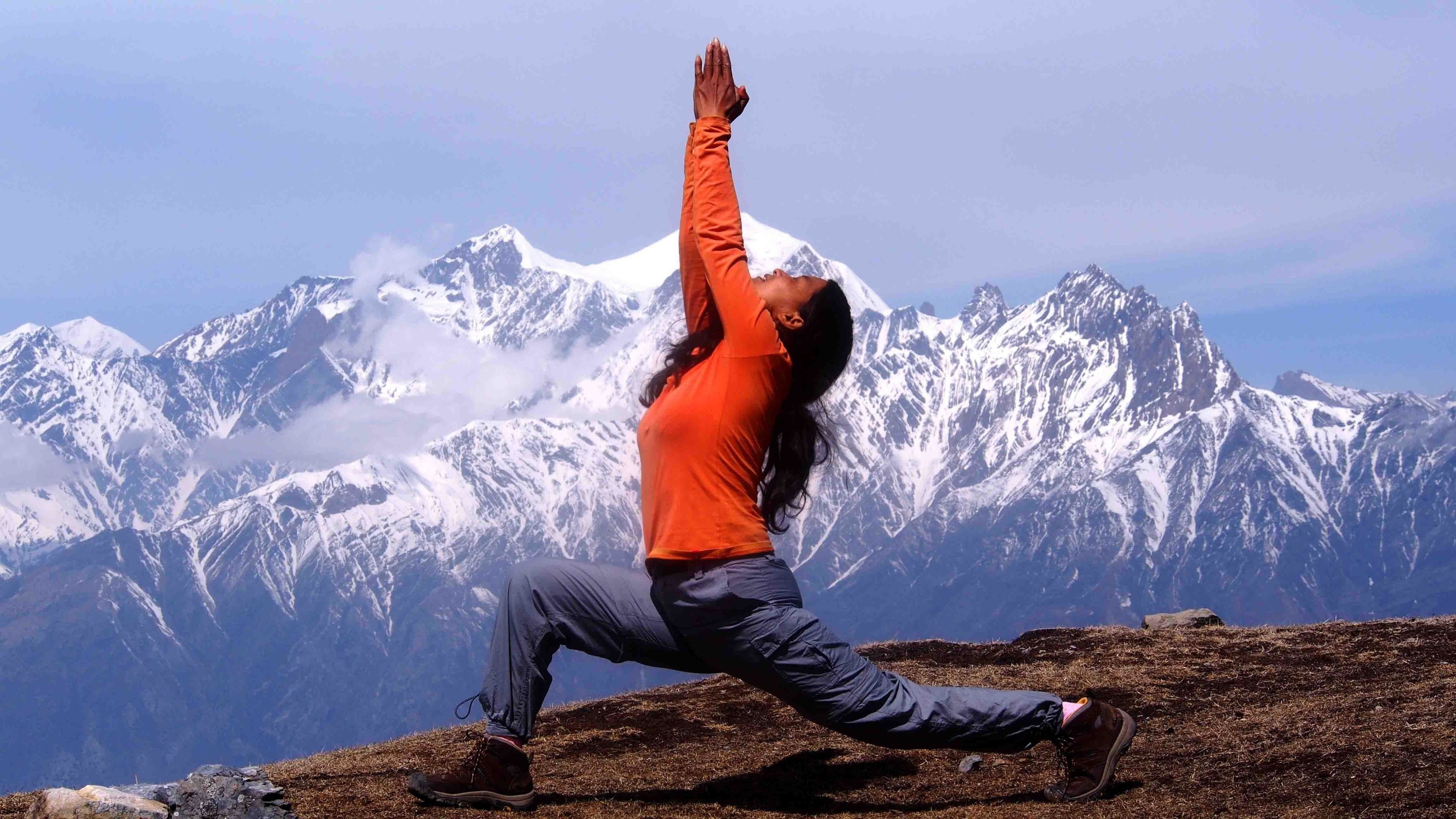A person performing a yoga pose on a rocky terrain with a mountain range in the background.
