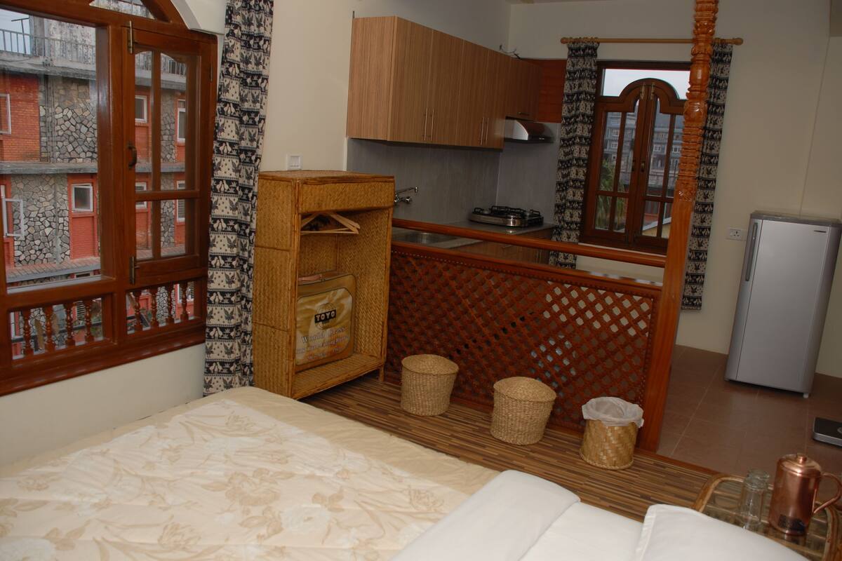 Een compacte kamer met een bed, een klein kitchenette en een raam met uitzicht op een gebouw.