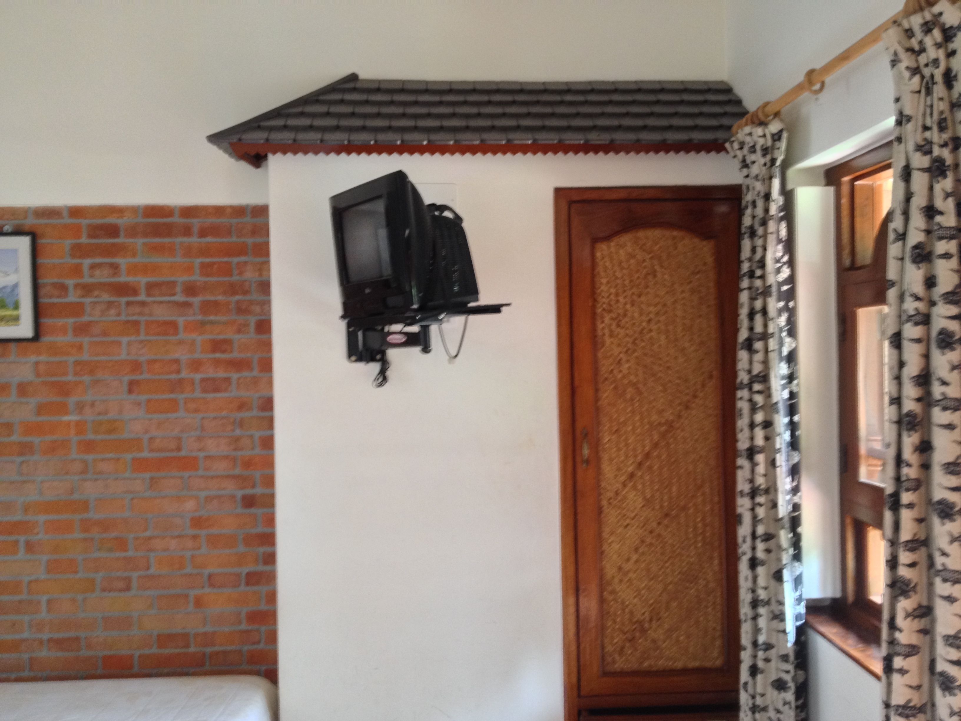 A room with a brick wall, a wooden door, and a television mounted on the wall.