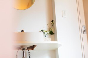 A bathroom with a white sink, a mirror, and a small vase with flowers.