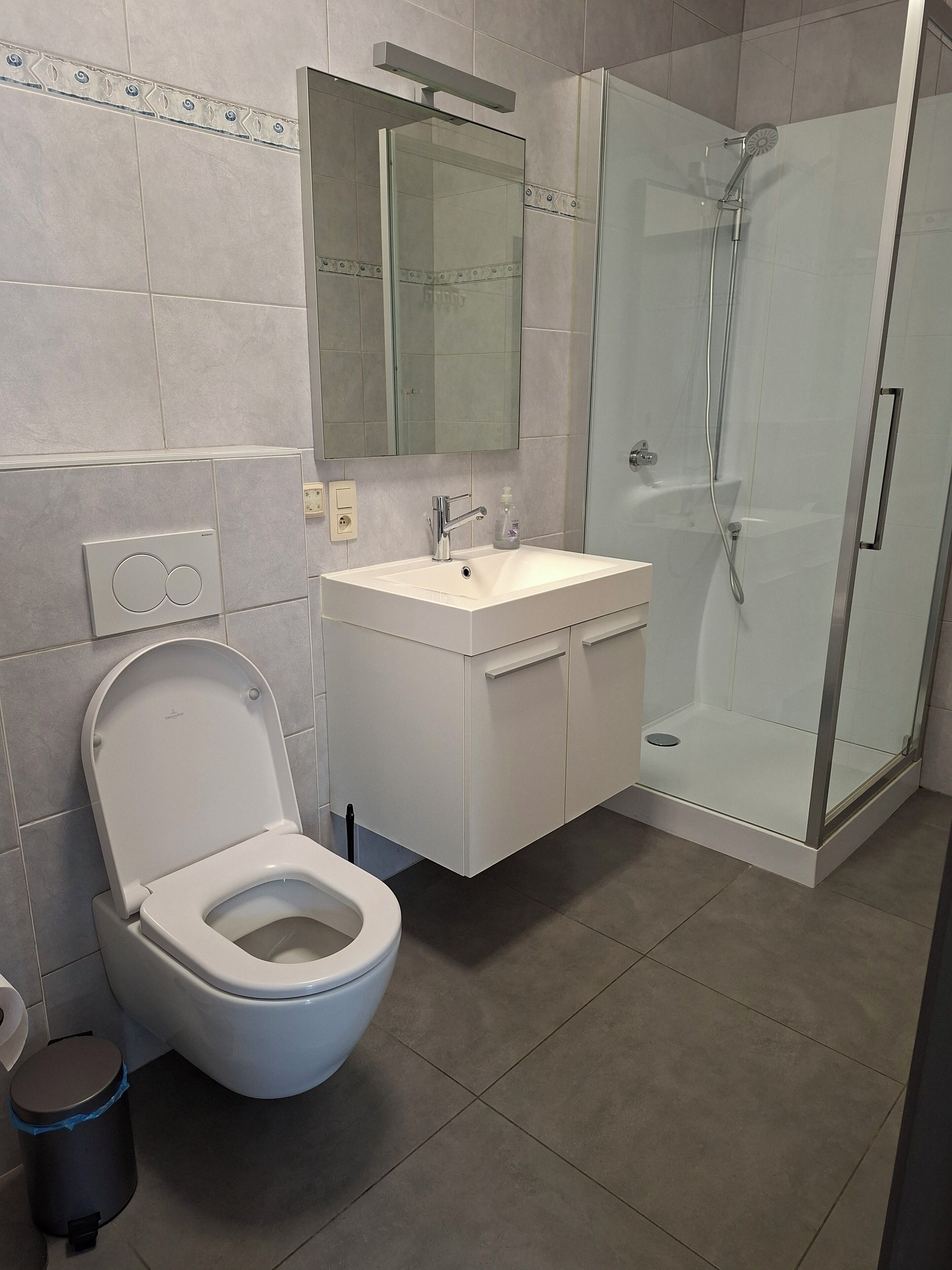 Un baño moderno con inodoro, lavabo, espejo y ducha con mampara de vidrio.
