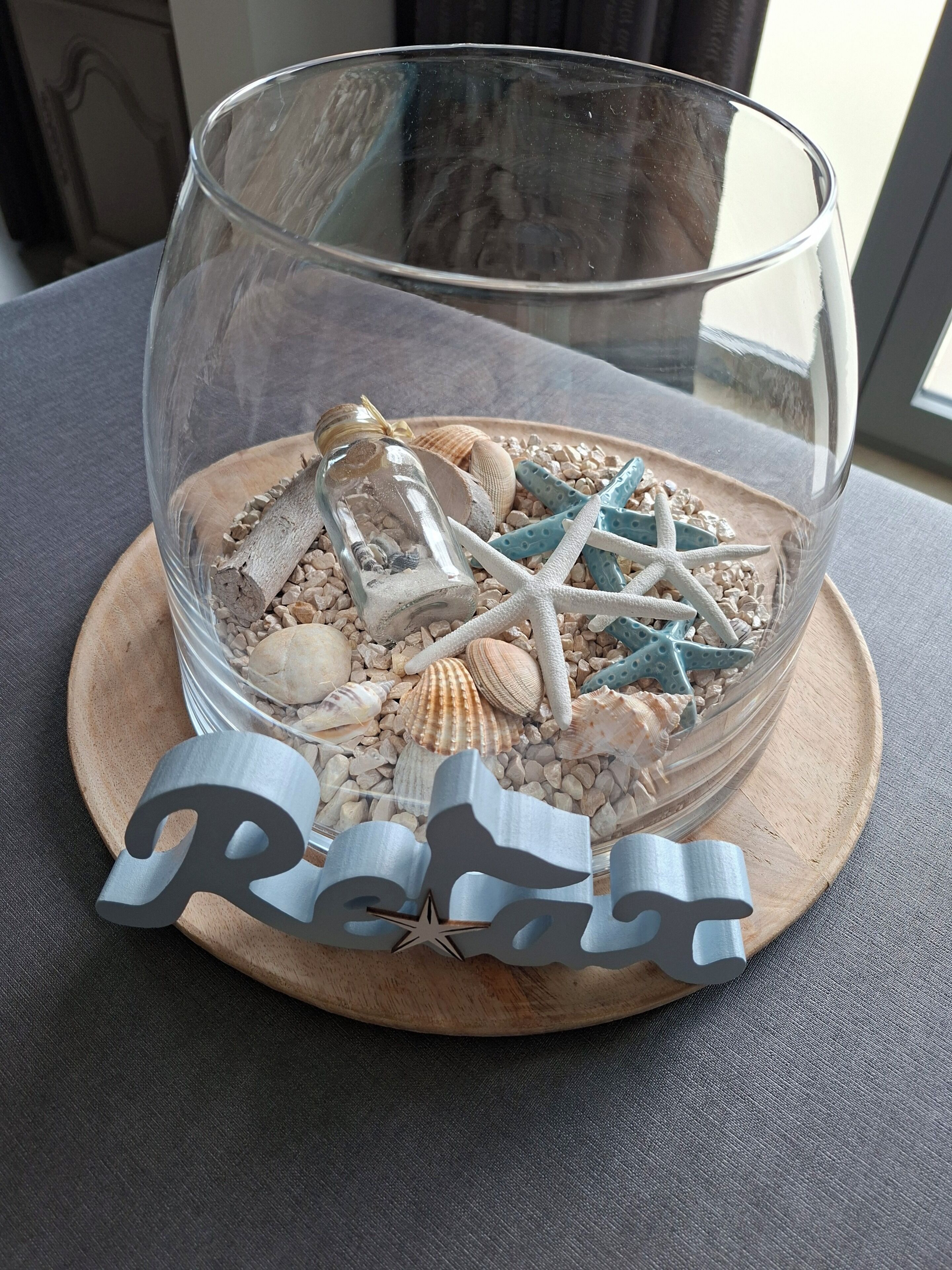 A glass bowl with seashells and starfish on a wooden coaster with the name 'Rita' cut out.