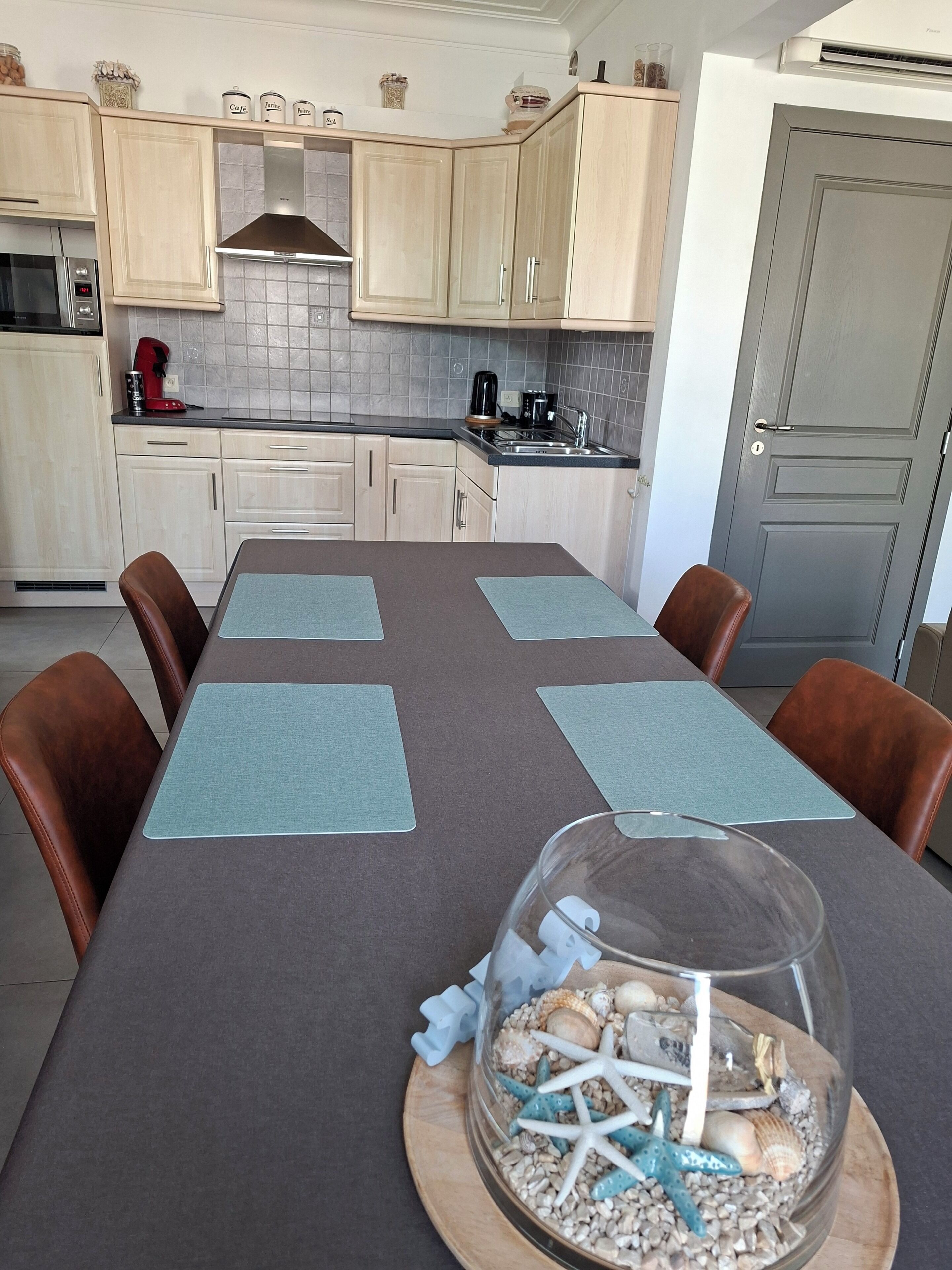 Cocina moderna con alacenas de madera clara, extractor de acero inoxidable y comedor con mesa para cuatro.