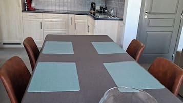 Cocina moderna con alacenas de madera clara, extractor de acero inoxidable y comedor con mesa para cuatro.