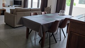 A modern living room with a dining area, a sofa, a flat-screen TV, and a balcony with curtains.