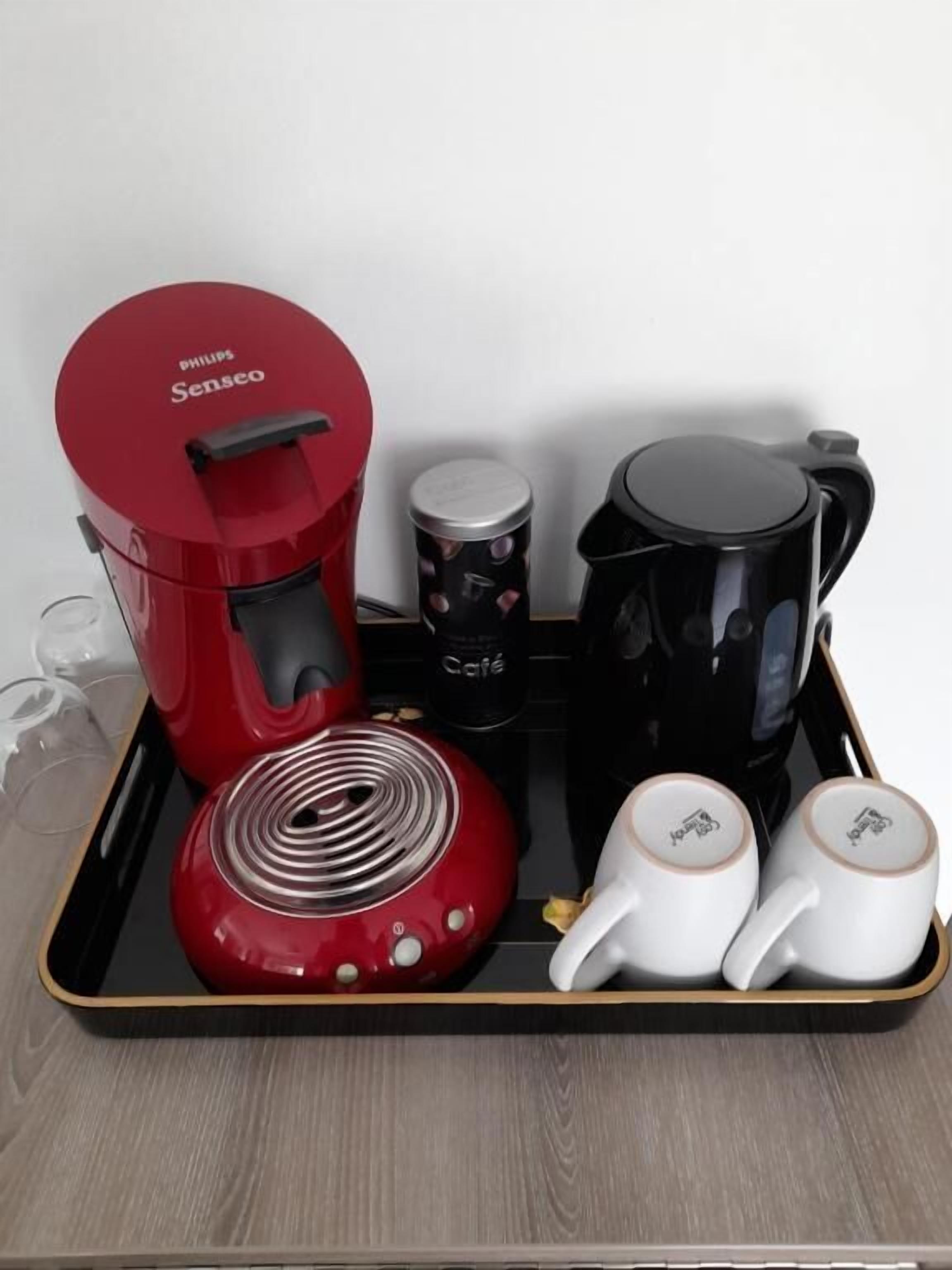 Ein Tablett mit einer roten Philips Senseo-Kaffeemaschine, einer schwarzen Kaffeekanne, einem schwarzen Behälter mit der Aufschrift 'Café' und zwei weißen Kaffeetassen.