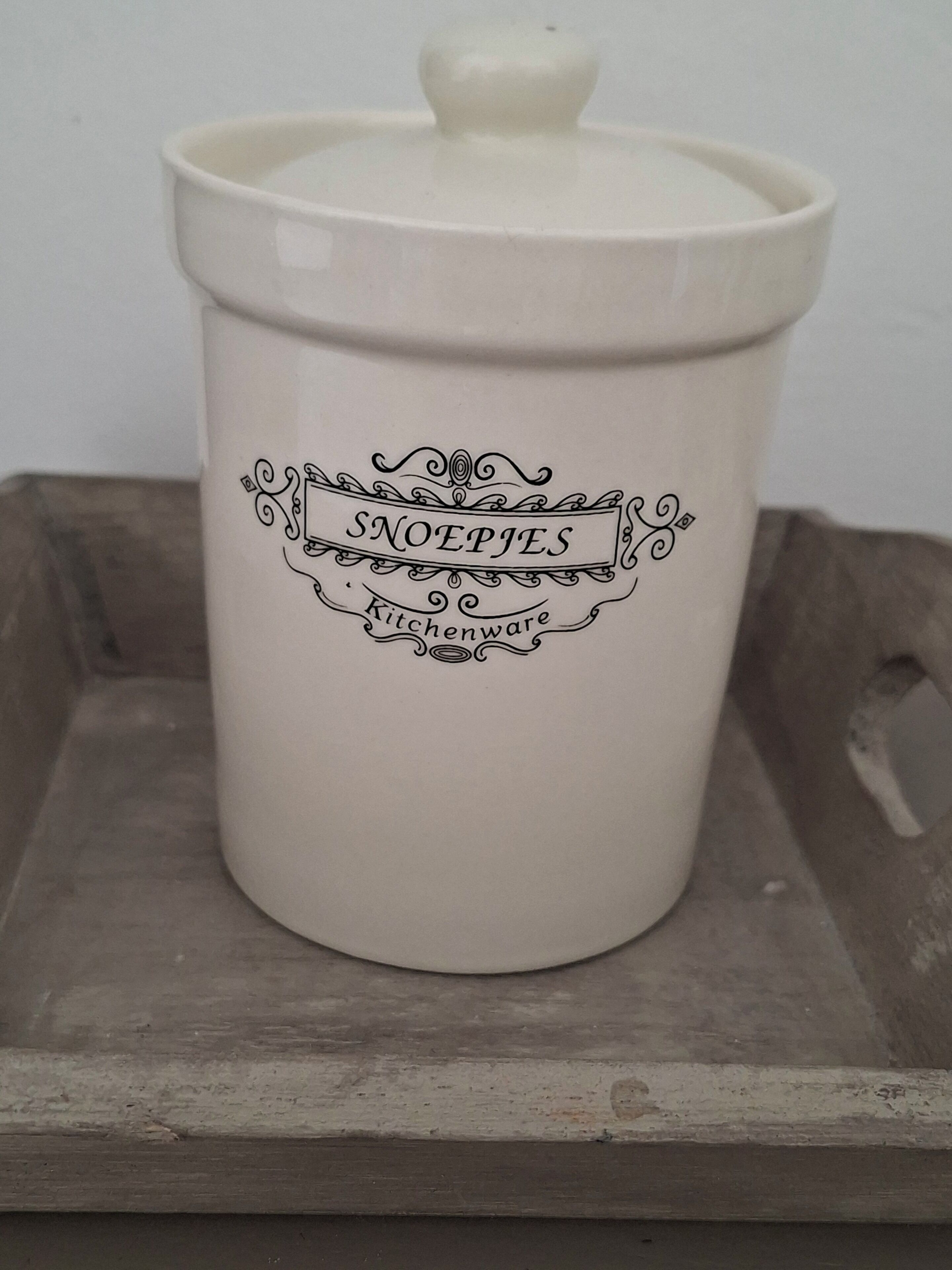 A white ceramic container with a lid, featuring decorative text and a handle.