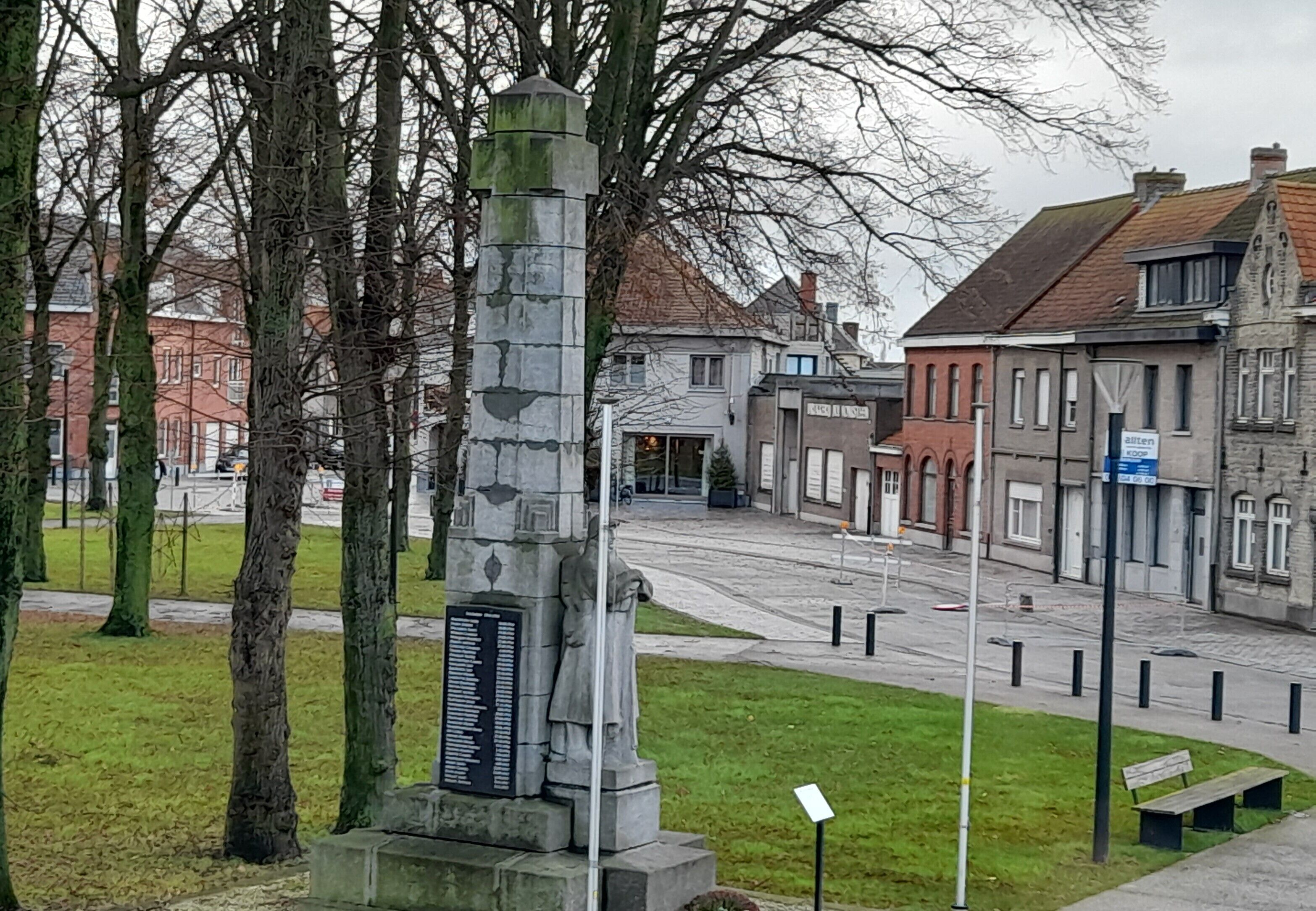Ein Denkmal mit einer Gedenktafel, umgeben von Bäumen und Gebäuden.