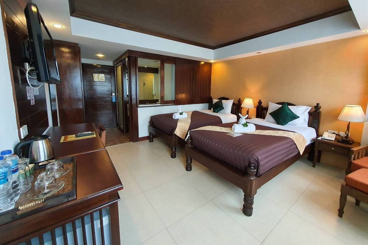 A hotel room with two beds, a desk with a kettle, and a mirror.