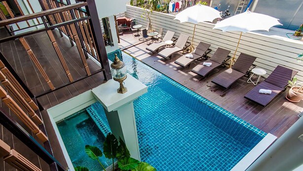 Ein Pool auf dem Dach mit Liegestühlen und Sonnenschirmen, umgeben von Holzterrasse und Topfpflanzen.