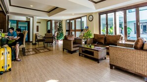 Eine geräumige Lobby mit hoher Decke, großen Fenstern und einem Weihnachtsbaum. Es gibt mehrere Sitzbereiche mit Korbmöbeln und einem Couchtisch.