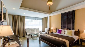 Ein Hotelzimmer mit einem großen Bett, einem Schreibtisch mit Stuhl, einer Couch und einem Fenster mit Vorhängen.