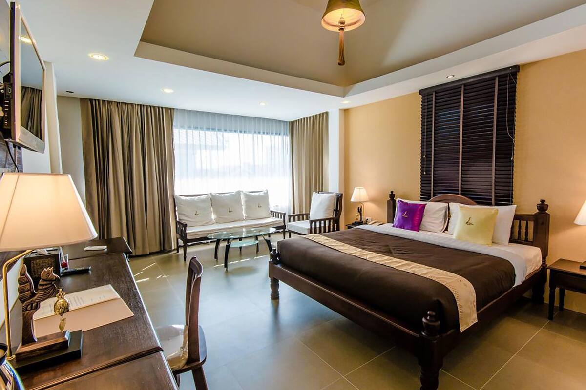 A hotel room with a large bed, a desk with a chair, a sofa, and a window with curtains.