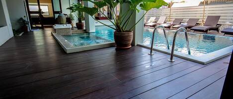 A pool area with two separate pools, lounge chairs, and potted plants.