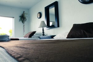 Un dormitorio con una cama, una mesita de noche con lámpara, un espejo y una ventana con cortinas.