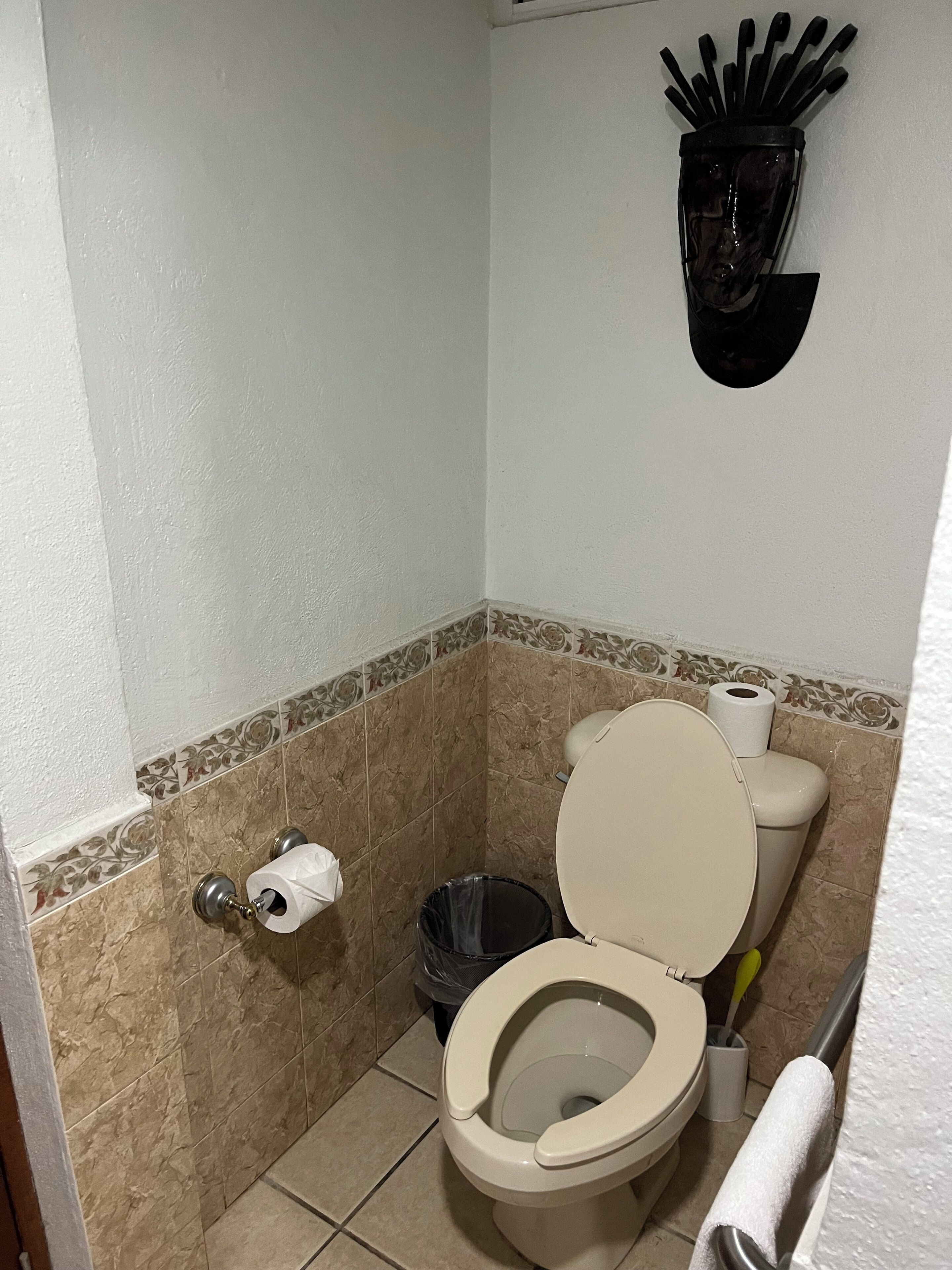 A small bathroom with a toilet, a trash can, and a toilet paper holder.