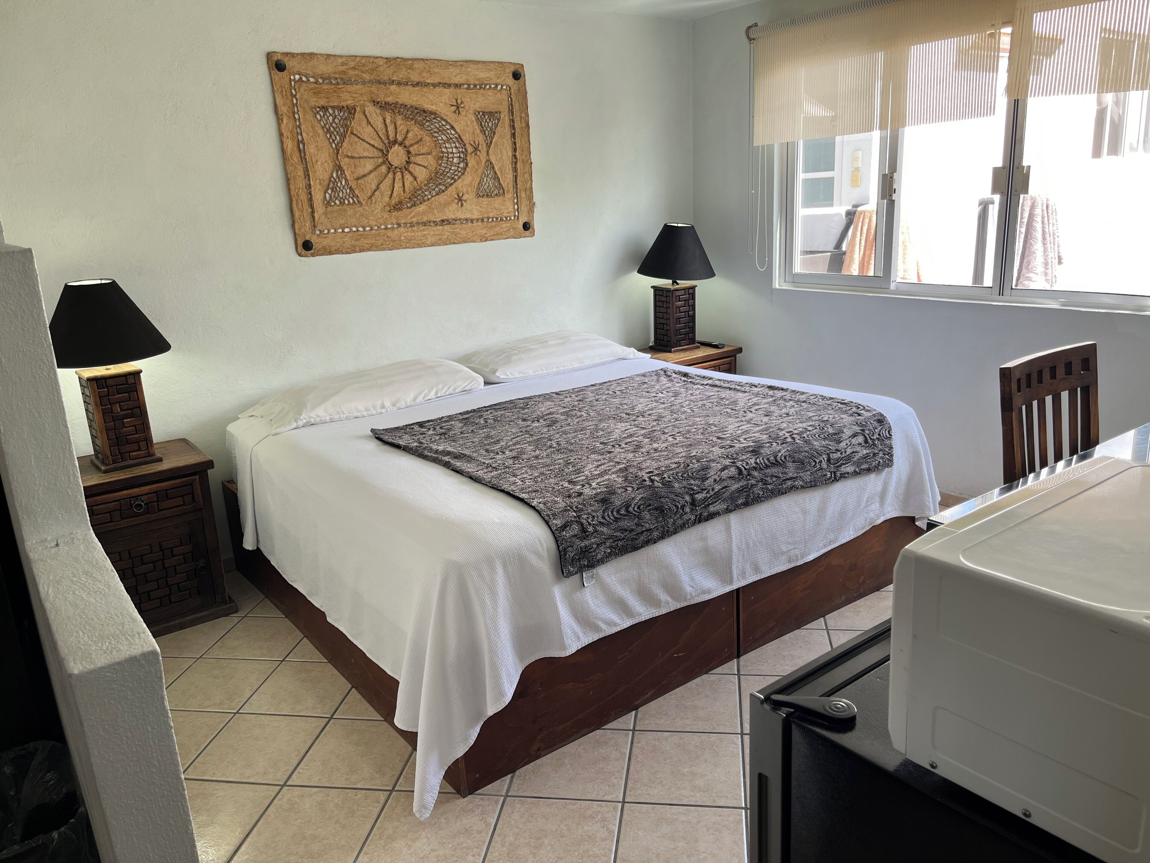 Une chambre à coucher avec un lit, deux tables de chevet avec des lampes, une décoration murale et une fenêtre avec des stores.