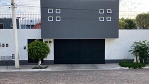 A modern building with a black garage door, a small tree, and a paved driveway. - Residencia Sofía (Querétaro)