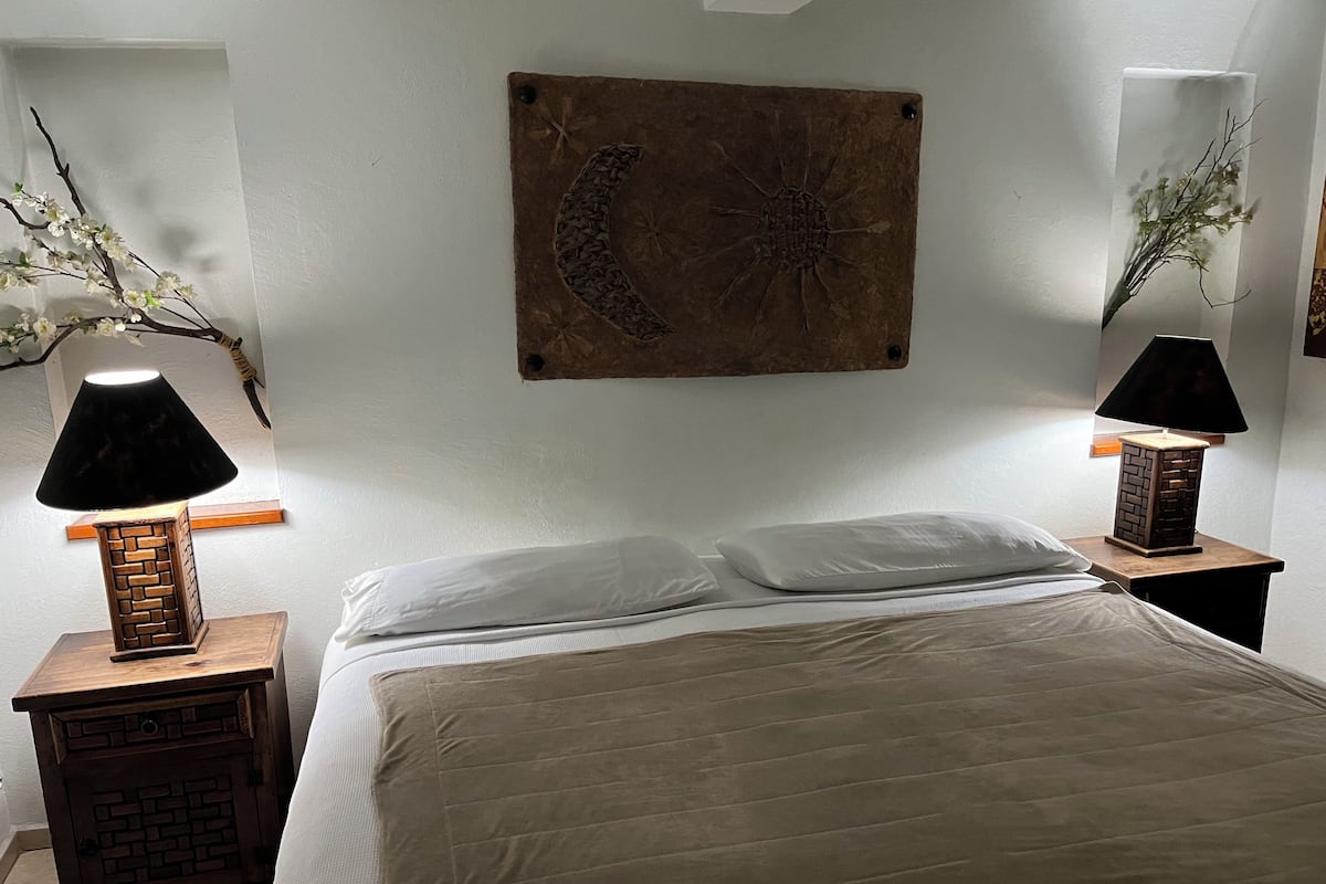 A neatly made bed with two white pillows, a wooden nightstand with a lamp, and a wall-mounted decorative piece.