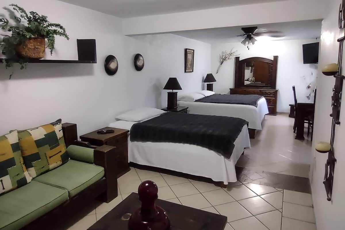 A hotel room with a sofa, two beds, a ceiling fan, a TV, and a mirror.