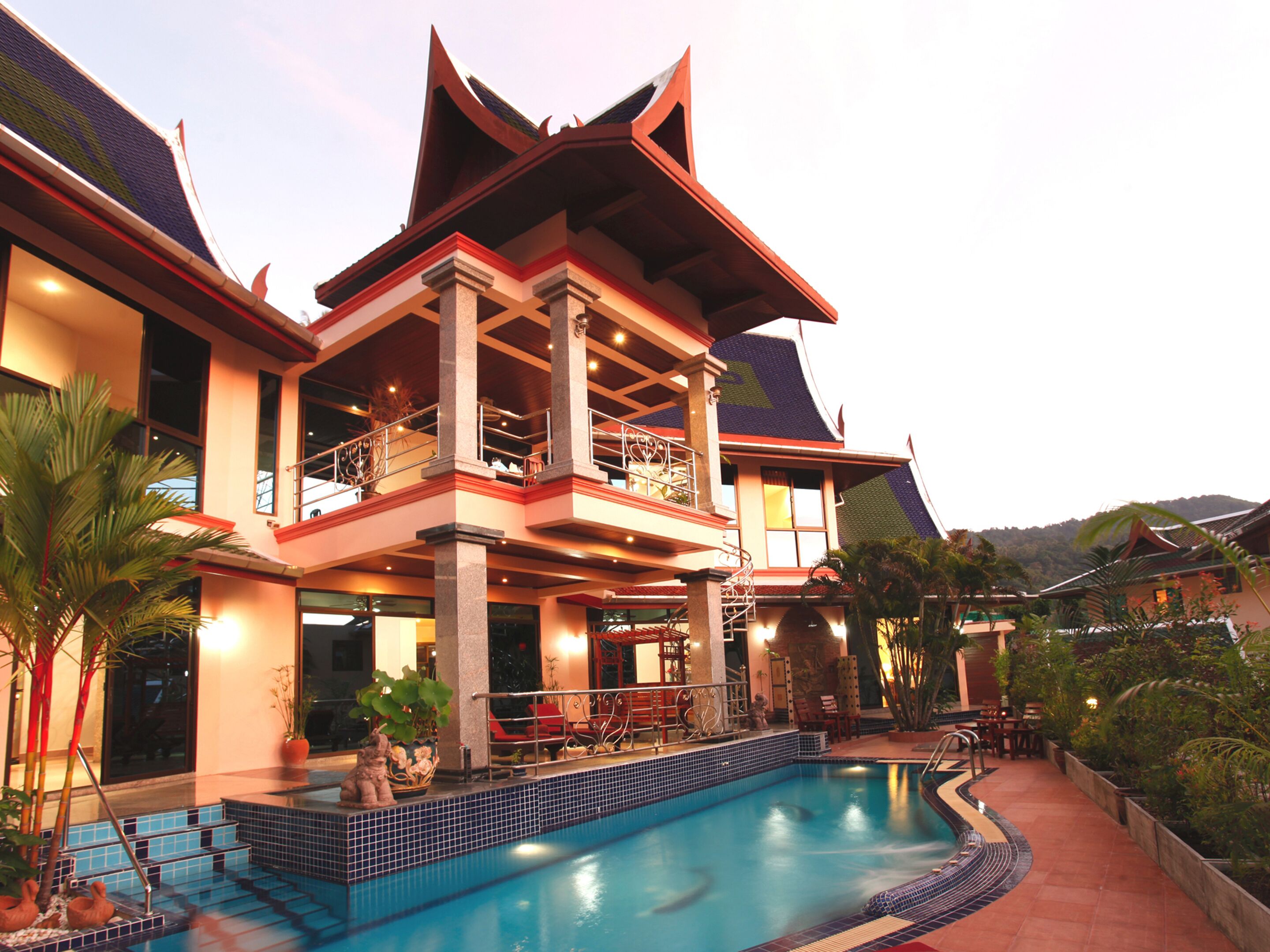 A large, multi-story building with a swimming pool, outdoor seating, and a mountainous backdrop.