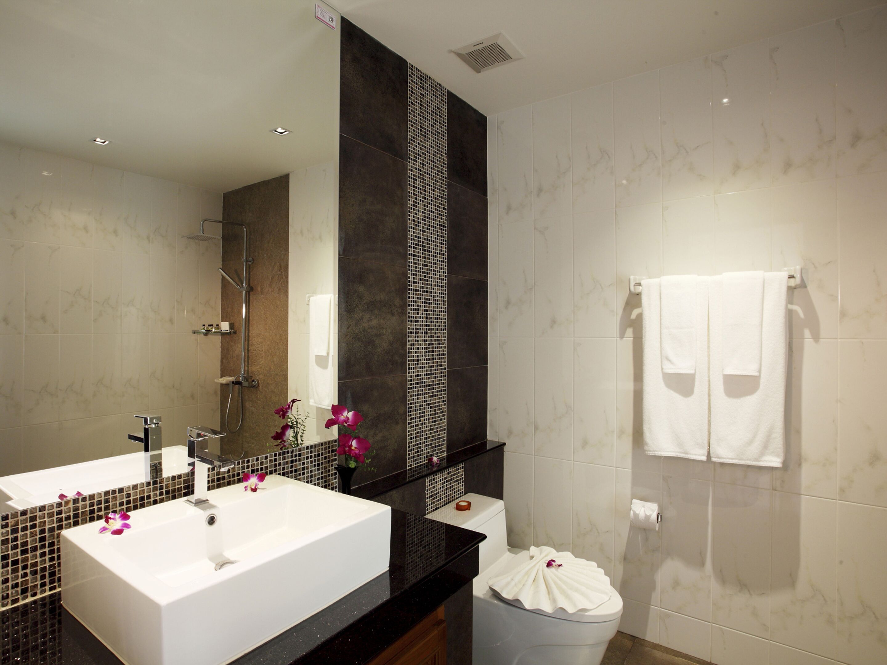 A modern bathroom with a large mirror, two sinks, a shower, and a toilet.