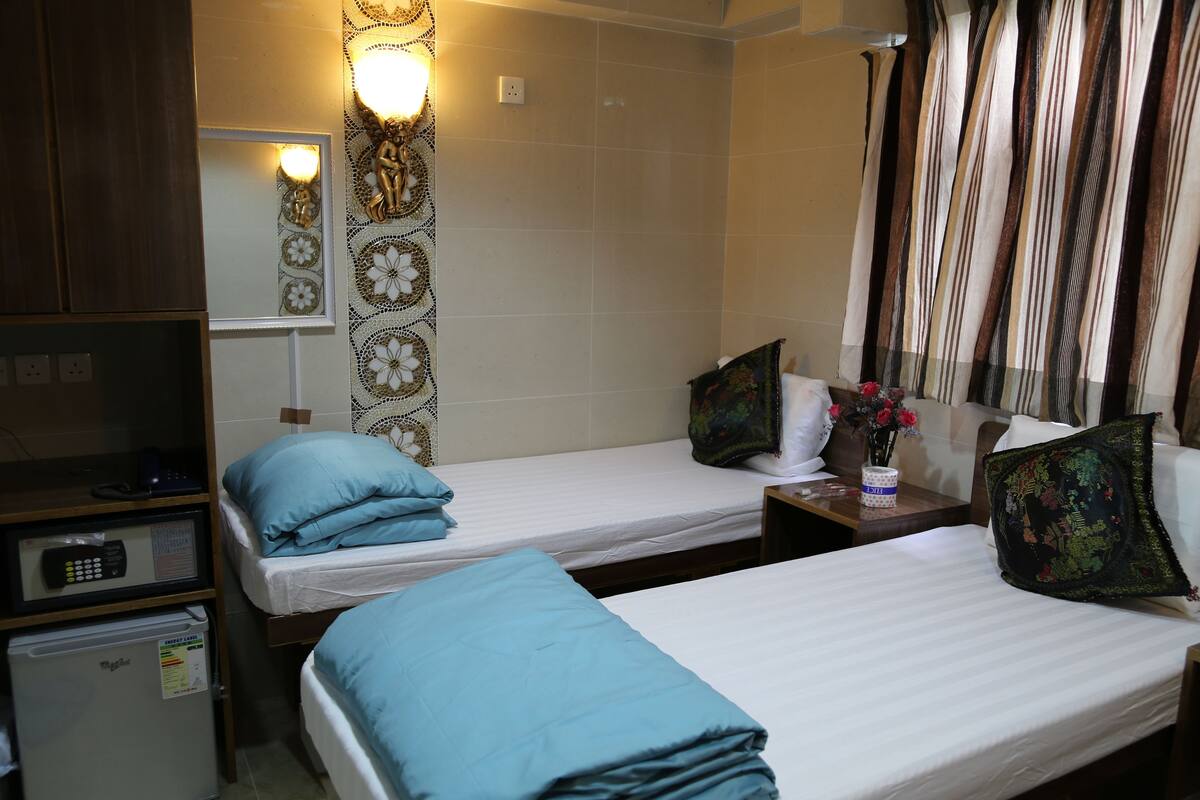 A hotel room with two single beds, a small desk with a telephone, and a minibar.