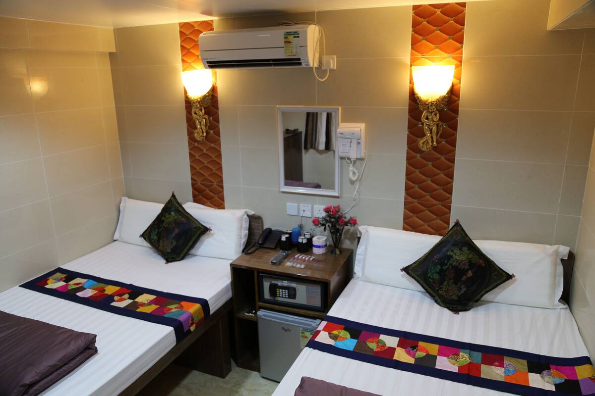 A hotel room with two beds, a small desk, a refrigerator, and a wall-mounted air conditioner.