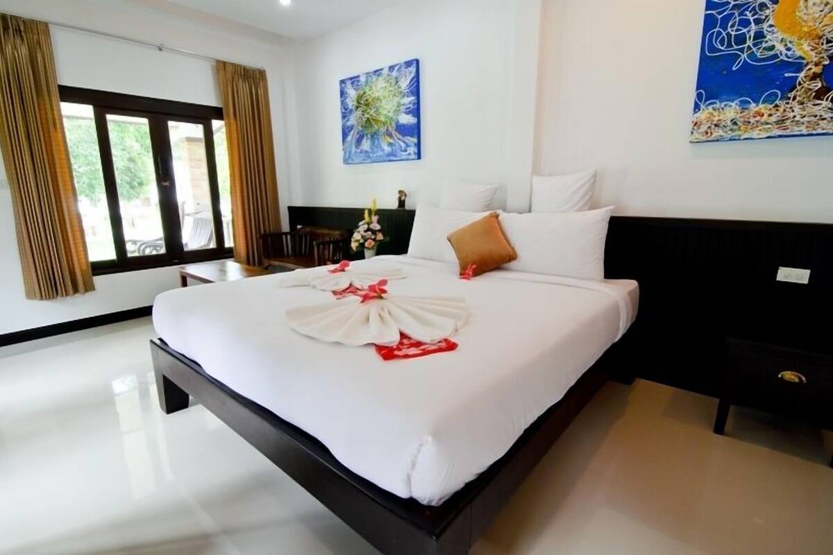 A hotel room with a large bed, a nightstand, a desk, and a chair. There are curtains on the window and a painting on the wall.