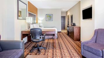 A hotel room with a bed, desk, chair, and a TV.