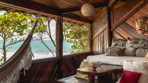 A wooden room with a bed, a hammock, and a view of the ocean. - Pousada Sage Point (Itacaré)