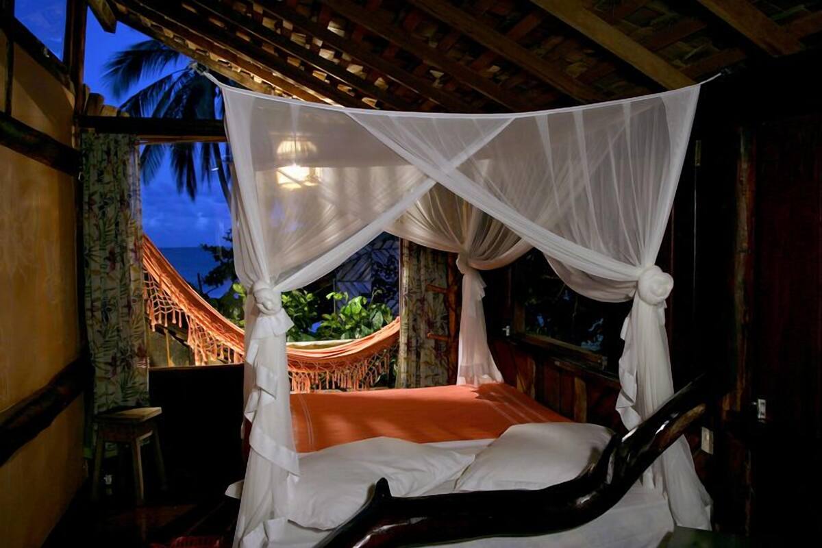 A four-poster bed with a canopy, a hammock, and a view of the ocean.