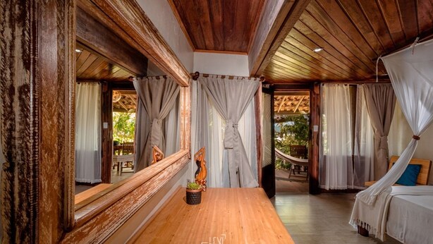 A wooden-floored room with a bed, a hammock, and curtains. - Pousada Sage Point (Itacaré)