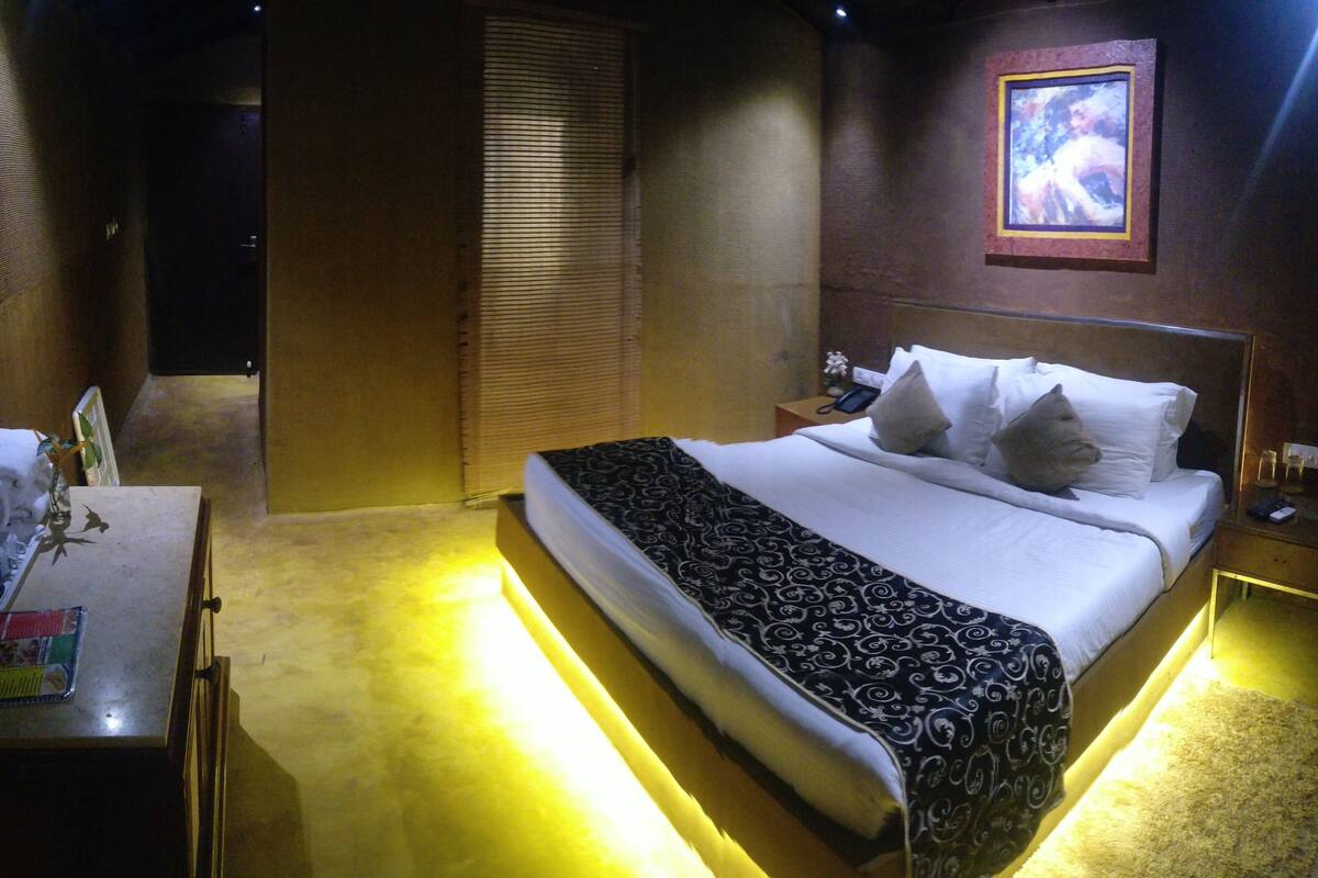 A hotel room with a bed, bedside table, lamp, and a painting on the wall.