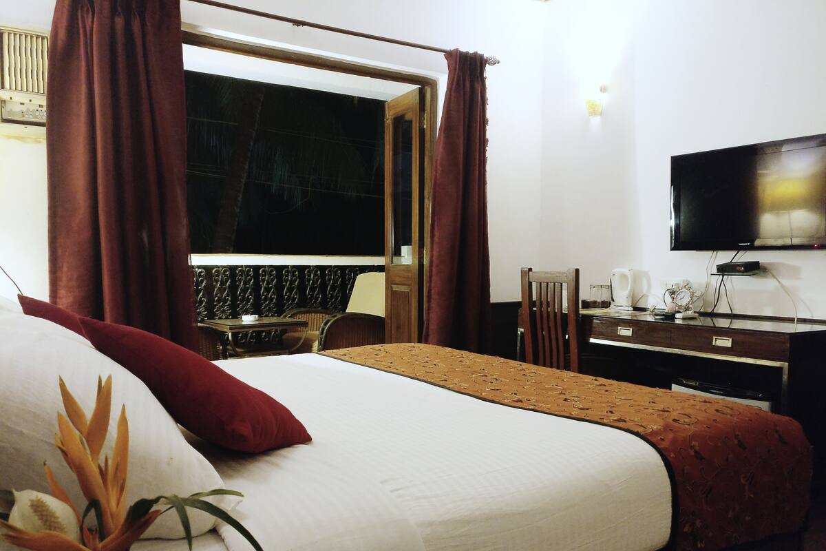 A hotel room with a large bed, a television mounted on the wall, and a window with curtains.