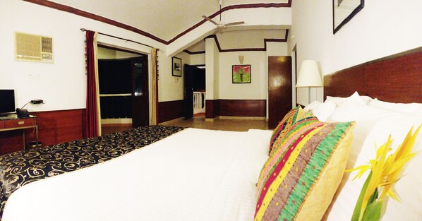 A hotel room with a large bed, a desk with a computer, a chair, a lamp, and a window with curtains. - The Camelot Beach Resort (Calangute)