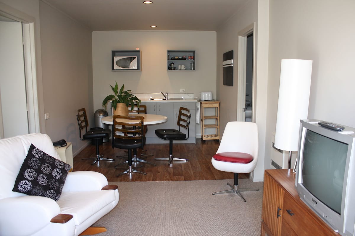 Una sala de estar con un sofá blanco, una televisión y un comedor con una mesa y sillas.