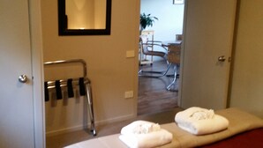 Et hotelværelse med seng, håndklædetørrestativ, spejl og udsigt til et spiseområde med bord og stole.