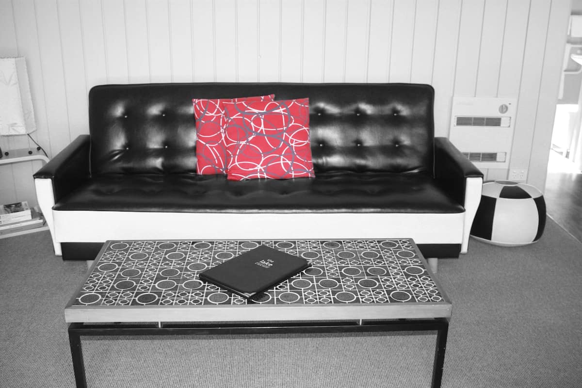 Una sala de estar moderna en blanco y negro, con un sofá de cuero negro, una mesa de centro con estampado y una almohada roja.