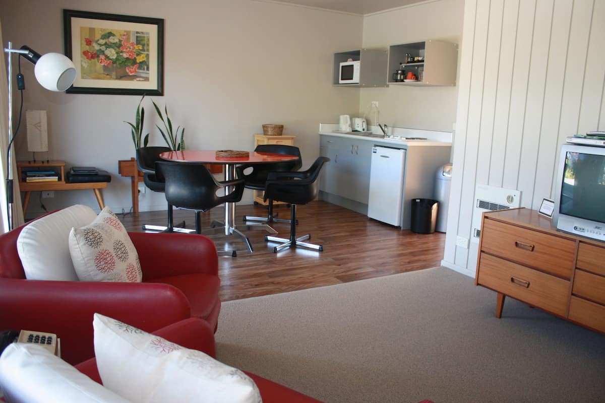 Un espacio habitable compacto con un sofá rojo, una mesa de comedor con sillas, una kitchenette y un televisor.