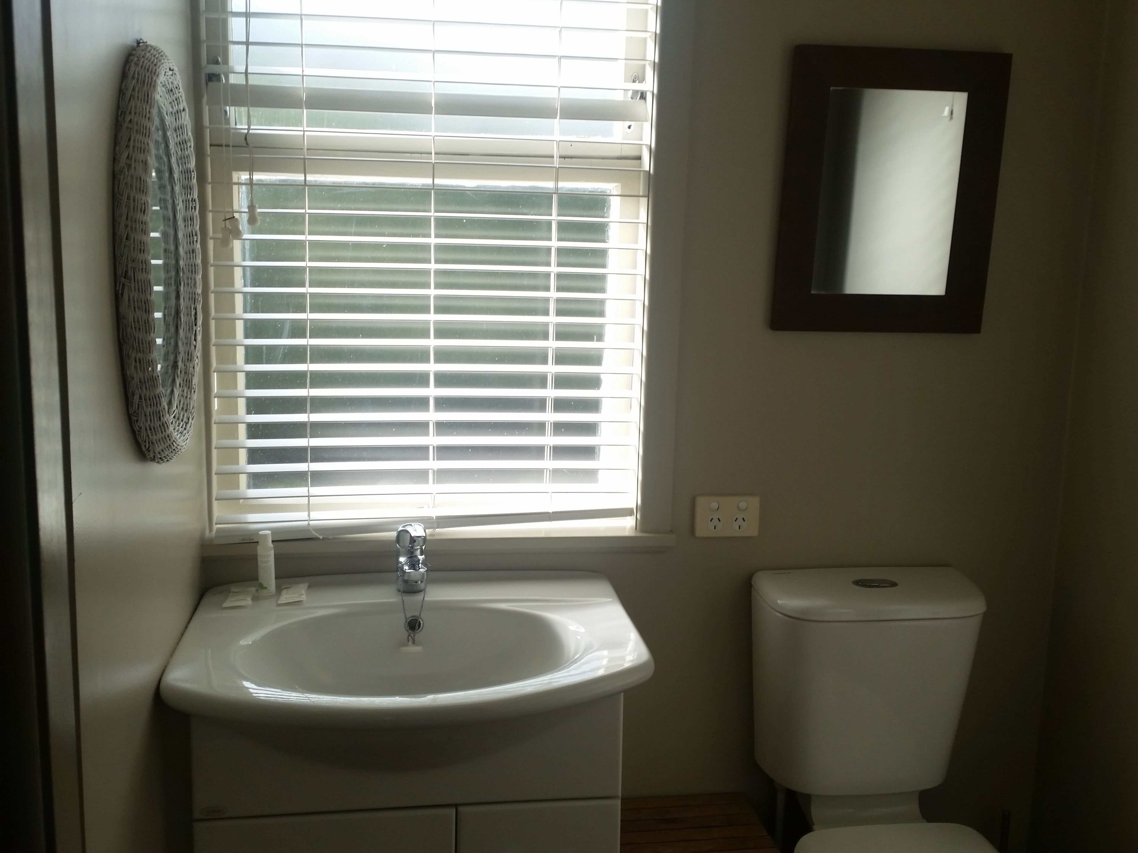A bathroom with a white sink, a toilet, and a window with blinds.