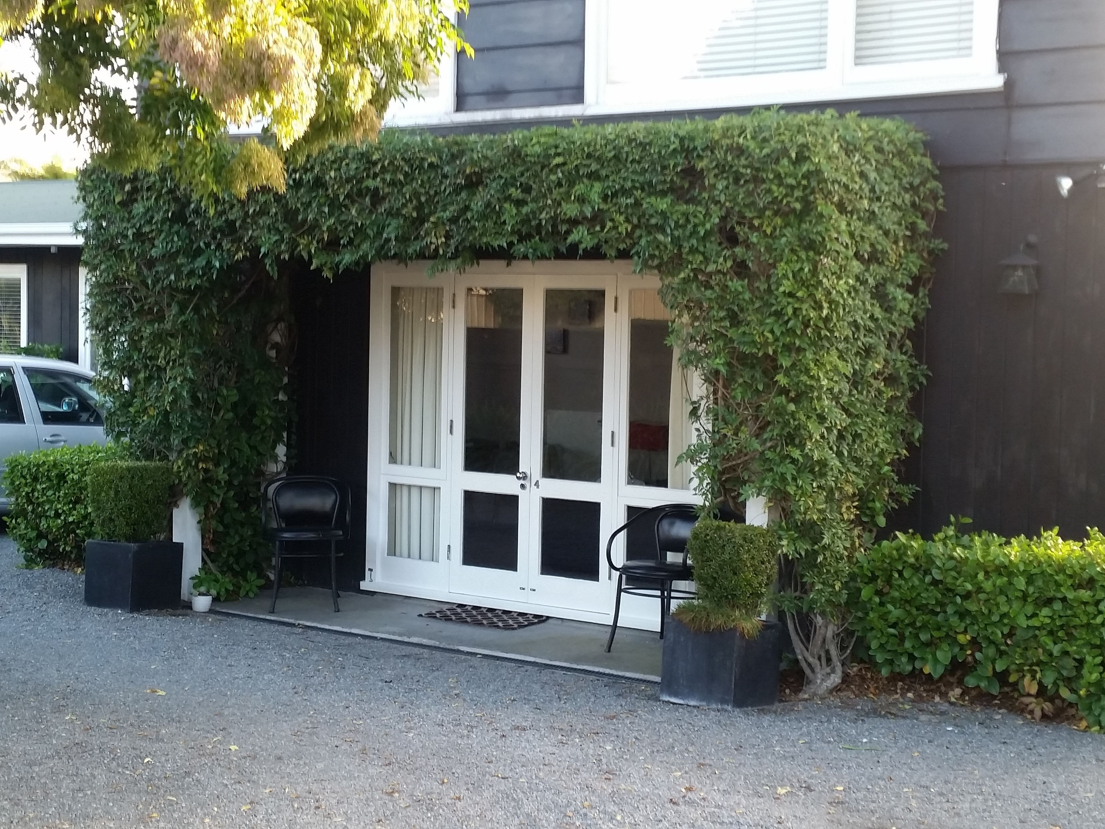 A building with a covered entrance, two chairs outside, and a potted plant.
