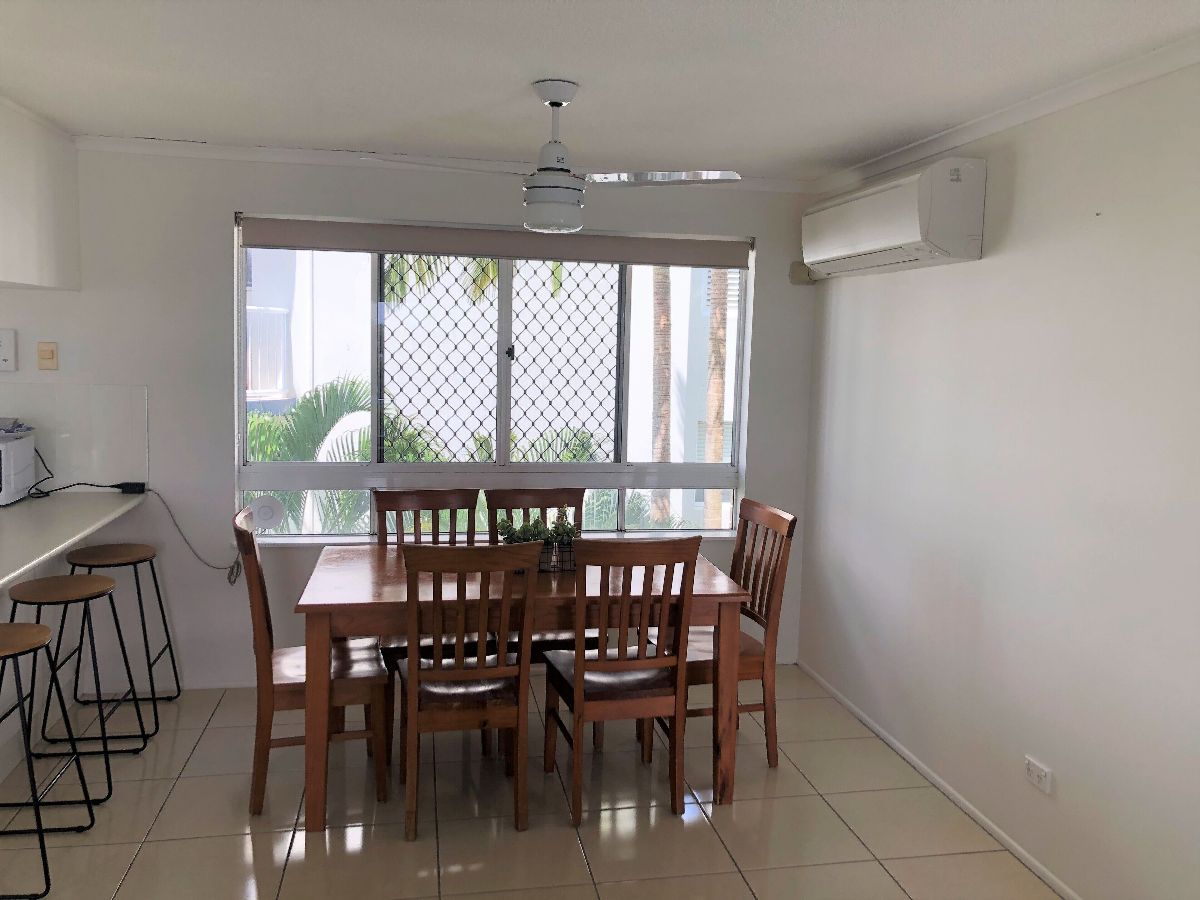 A dining area with a table and chairs, a ceiling fan, and a large window with a view of palm trees.