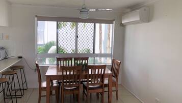 A dining area with a table and chairs, a ceiling fan, and a large window with a view of palm trees.