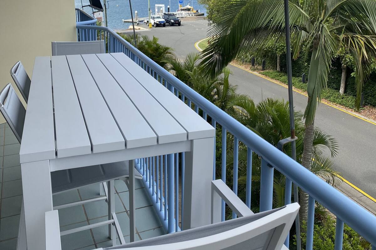 A balcony with a white table and chairs, overlooking a marina with boats and a clear sky.