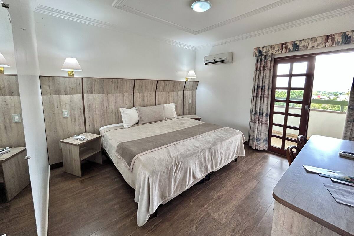 Habitación de hotel con una cama grande, mesitas de noche, un escritorio y un balcón con vistas.